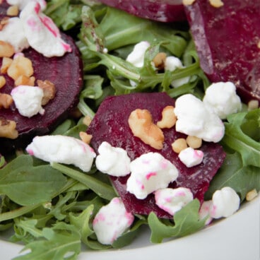 A close up of sliced beets, arugula, crumbled goat cheese, and chopped walnuts.