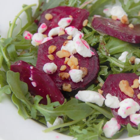 Close up of sliced red beets on a bed of arugula sprinkled with goat cheese and walnuts.