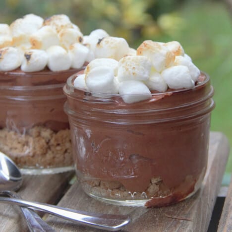 Close up shot of two small glass canning jars holding chocolate mousse and topped with browned mini marshmallows.