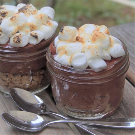 Two small canning jars are filled with chocolate mousse and topped with browned marshmallows.