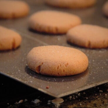 A close up of a baked ginger snap cookie on a baking sheet, with more cookies in the background.