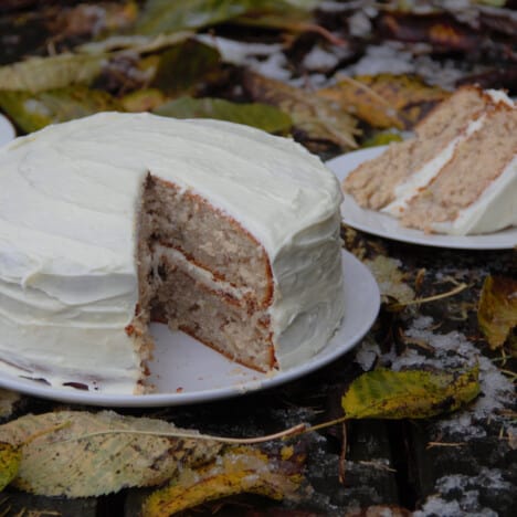 A whole frosted hummingbird cake with a slice removed and on a plate.