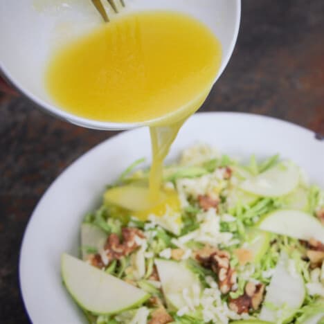 A fresh dressing being poured onto a salad containing apple and walnuts.