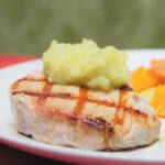 A pork chop with grill marks topped with apple sauce.