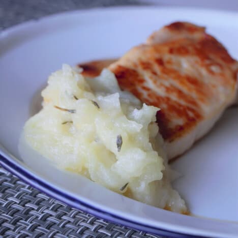 Apple sauce with thyme and a pork chop sitting on a white camp plate.