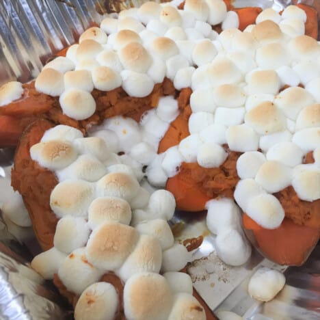 Looking down onto cooked sweet potatoes in a foil dish, covered in mini marshmallows.