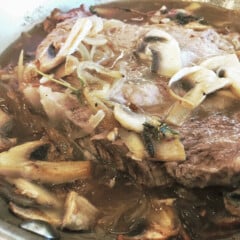 Close up of a braised steak covered in sliced mushrooms and sauce.
