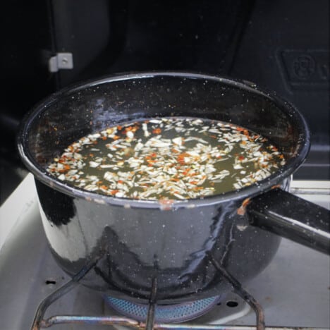 A black enamel saucepan on a camp stove with broth heating in it.