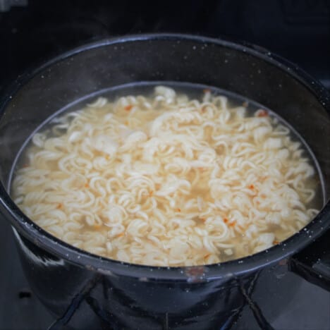 A black saucepan with soft noodles in a broth.