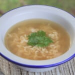 A white camp bowl with noodle soup topped with fresh cilantro.