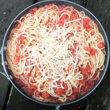 Looking down into a pot with spaghetti noodles, tomato sauce, and grated Parmesan cheese.