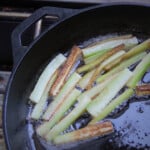 Looking down on cucumber frying in a skillet over a camp gas stove.