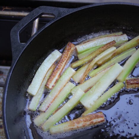 Looking down on cucumber frying in a skillet over a camp gas stove.