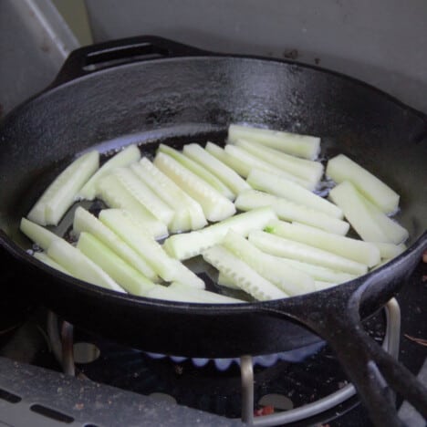 Raw cucumber sitting it a skillet over a camp gas stove.