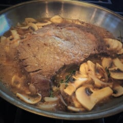 Looking into a saute pan with a braised steak and sliced mushrooms.