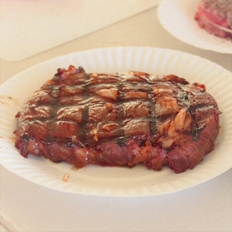 A cooked marinated steak with crisscross grill marks resting on a paper plate.