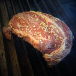 A marinated ribeye steak sitting on grill grates with finely diced garlic and ginger visible.