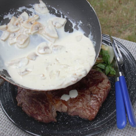 A small frypan starting to pour the mushroom sauce over the steak.
