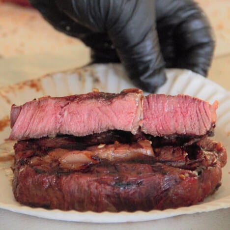 A halved rare cooked steak on a paper plate exposing the inside of one half and the cooked edge of the other half.