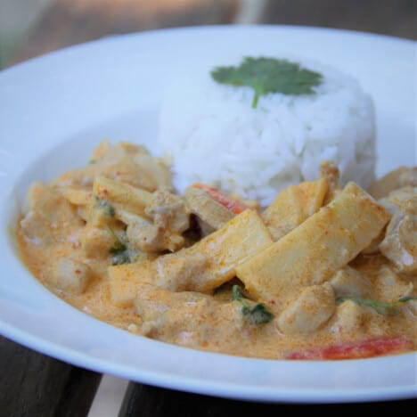 Looking into a white shallow bowl with Thai red curry and cooked white rice.