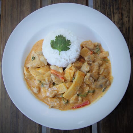 Looking down into a shallow white bowl with a serving of Thai red curry and white rice.