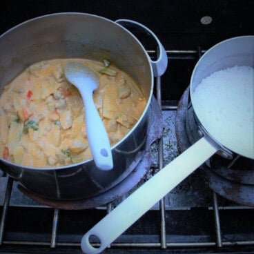 A pot of Thai red curry and a pot of white rice cooking on a camp stove.