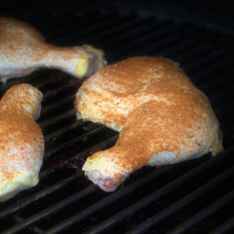 Raw chicken quarters with rub on them placed on a grill.