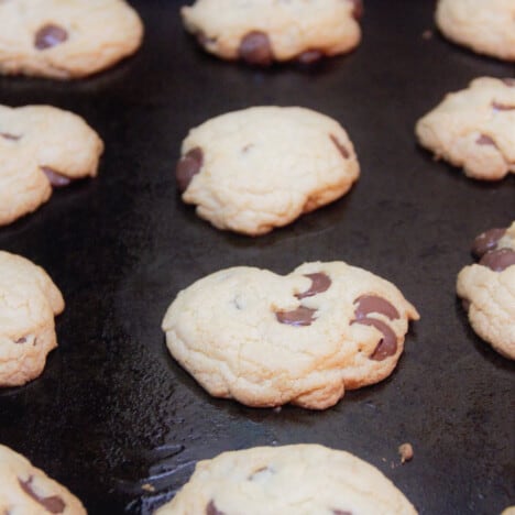 A row of freshly baked chocolate chips cookies line a black baking sheet.