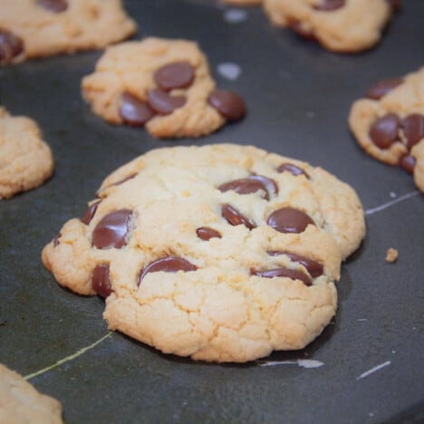 A freshly baked chocolate chip cookie sits on a black baking sheet.