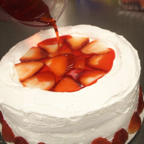 Strawberry jello being poured onto the top of the cake.