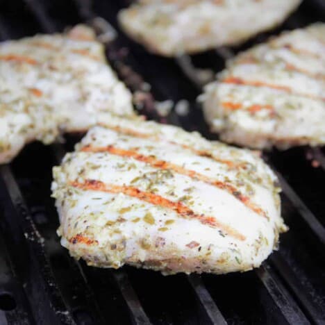 Seasoned chicken breasts are cooking on the grill.