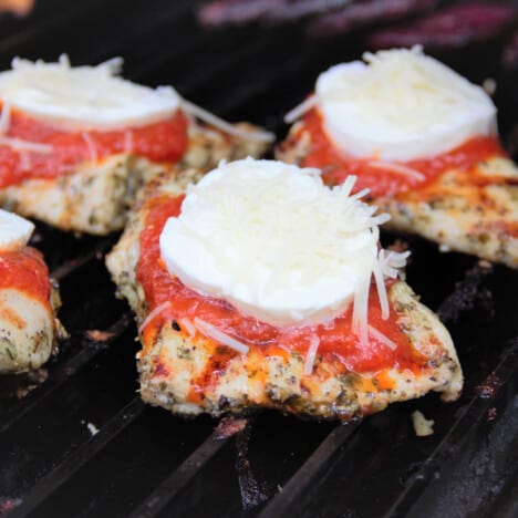 Grillgrates with grilled chicken that has recently been topped with pasta sauce, mozzarella, and Parmesan.