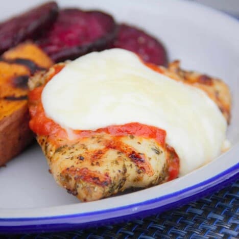 A white camp plate with grilled chicken parma and a side of sweet potato and beetroot.