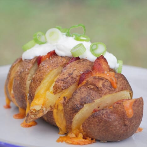A camp plate with a ready to each hasselback potato stuffed with bacon and cheese and topped with sour cream.