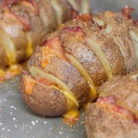 Close up of a hasselback potato stuffed with melted cheese and bacon and topped with a rub.