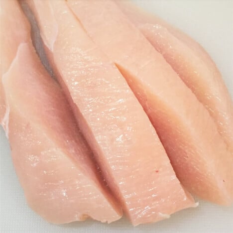 A raw chicken breast cut into strip slices.