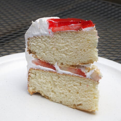 A slice of strawberry Danish cake on a white camp plate on a mesh picnic table.