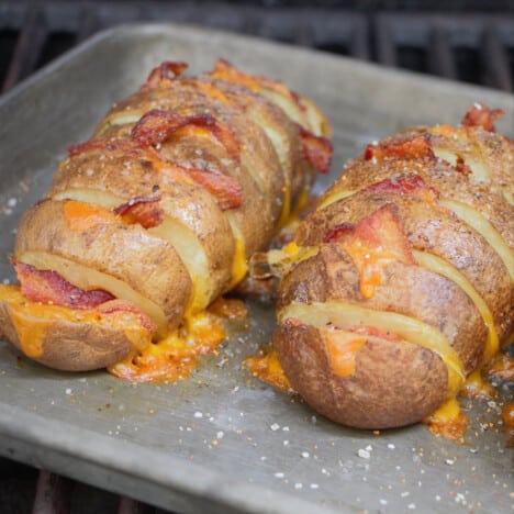 A baking tray with two hasselback potatoes stuffed with melted cheese and bacon.