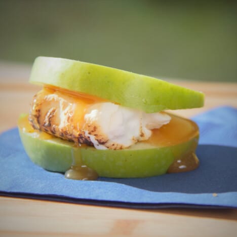 Close up of an apple smore with marshmallow and caramel sauce on a blue napkin.