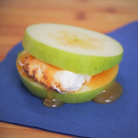 Looking down on an apple smore with marshmallow and caramel sauce oozing onto a blue napkin.