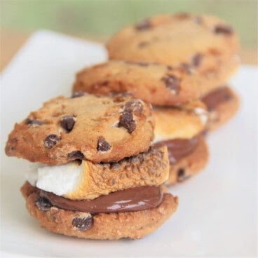 Three chocolate chip smore cookies are lined up on a white serving plate.
