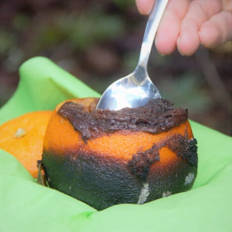 A spoon taking a scoop of chocolate cake from an orange resting in a green napkin.
