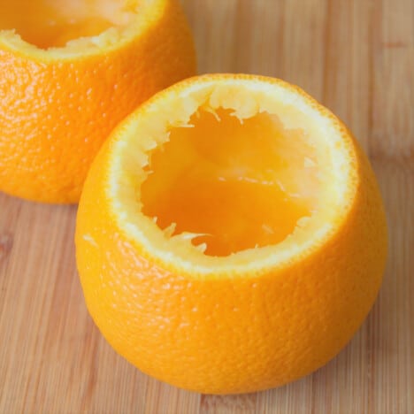 A hallowed-out orange sits on a wooden cutting board.