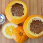 Two hallowed-out oranges filled with chocolate cake mix are resting on a wooden cutting board.
