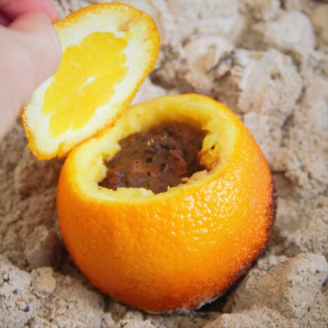 An orange is filled with chocolate cake batter sitting in hot coals.