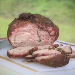 A muscle of lamb leg is slice on a chopping board showing the smoke ring and pink moist center.
