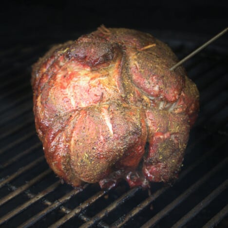 A boneless and trussed lamb almost finished smoking sitting on grill grates.