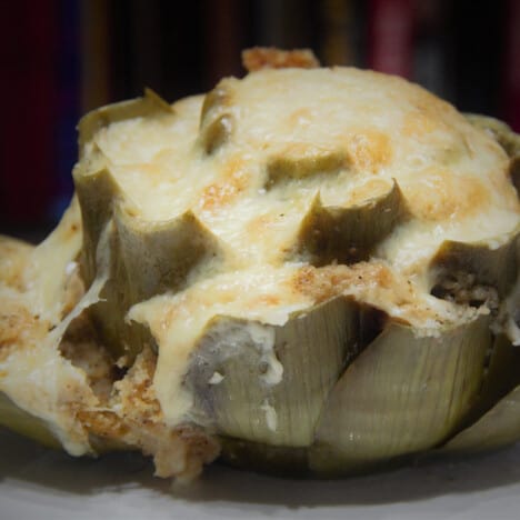 A steamed stuffed artichoke with cheese oozing out of it.