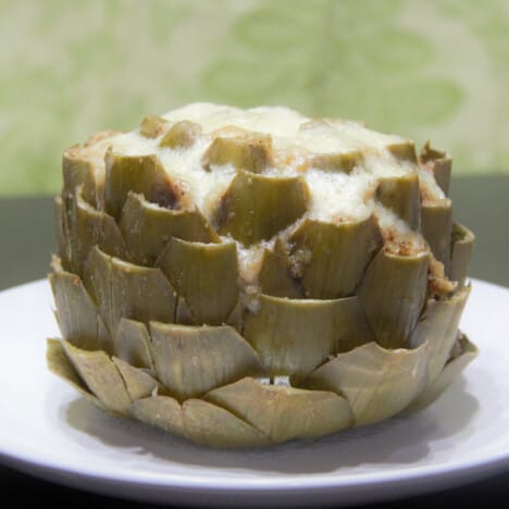 A stuffed artichoke sits on a white serving plate.