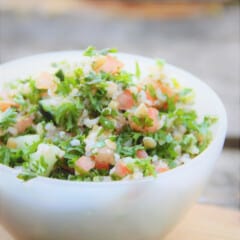 Looking into a white serving bowl filled with tabbouleh salad, on a wooden cutting board with a gray background.